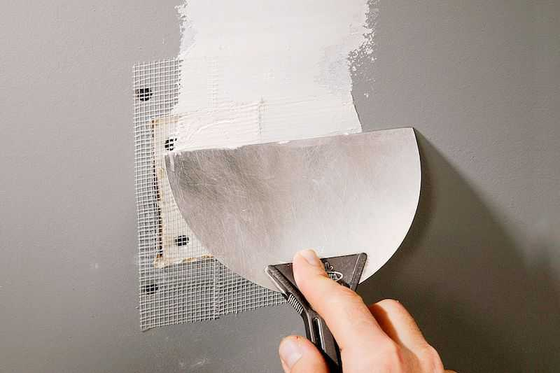 Smoothing joint compound over mesh tape during a drywall patch repair