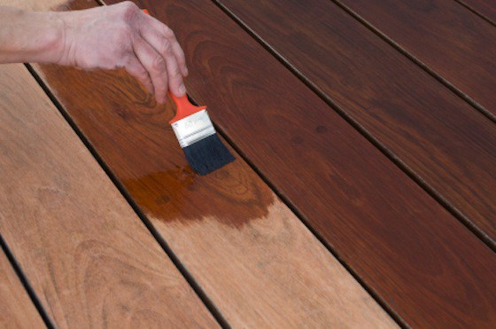 Hand applying wood stain to a deck board